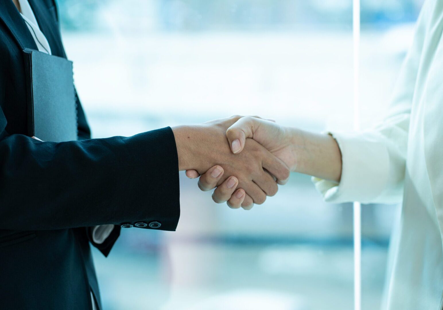 Close-up of two businessmen shaking hands while sitting in office. Successful partner.